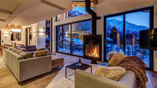 Ein modernes Wohnzimmer mit Kamin, großen Fenstern und Bergblick sowie einer gemütlichen Sitzecke.