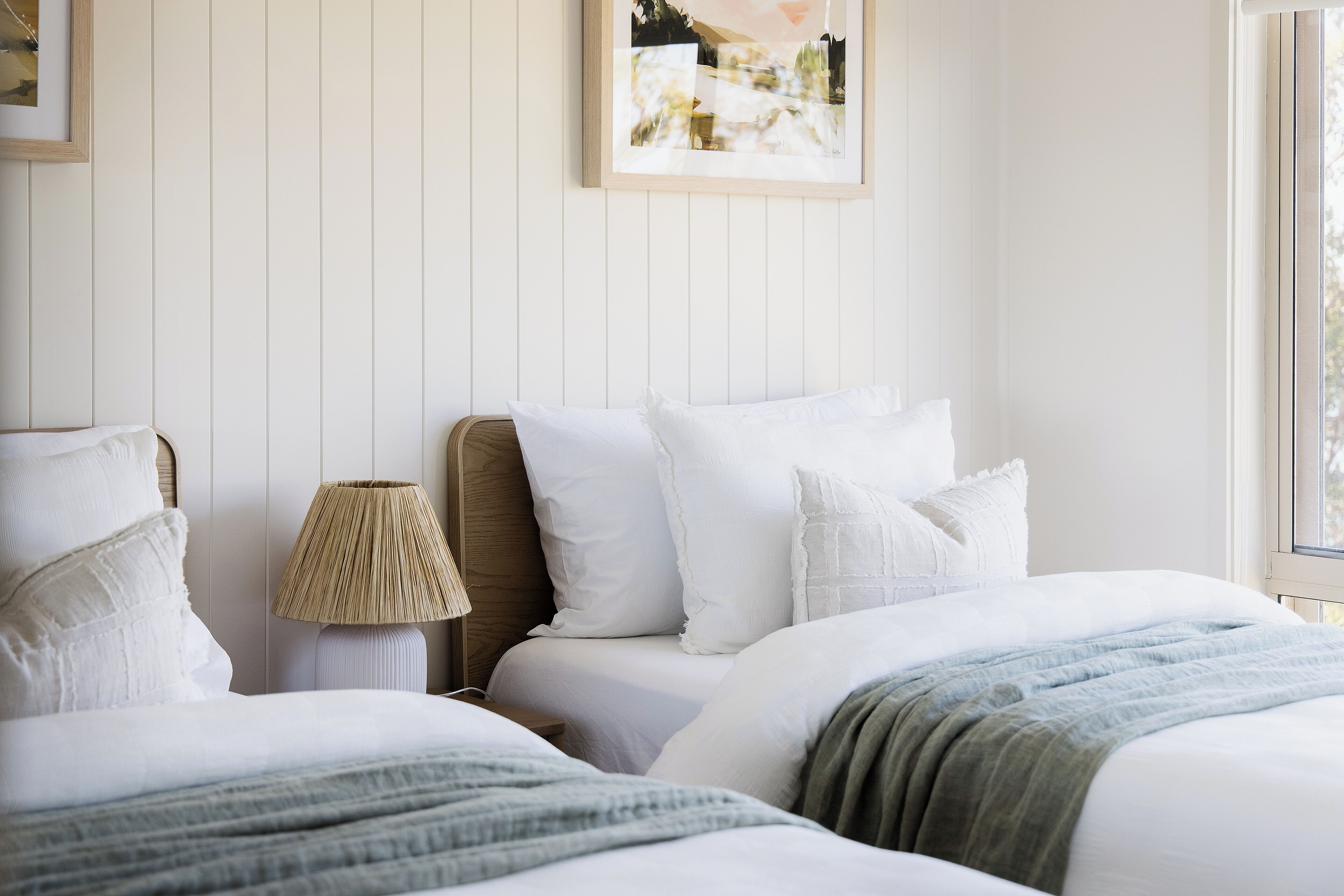 A bedroom with two beds, white bedding, a lamp, and a framed picture on the wall.
