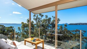 Un balcón con vista despejada al mar, una mesa de madera con comida y un sofá.