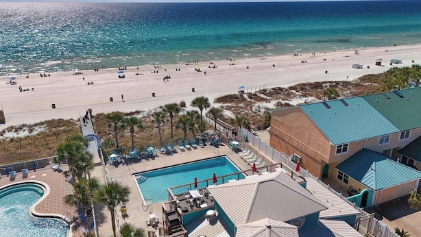 Un resort sulla spiaggia con piscina, lettini e vista sull'oceano.