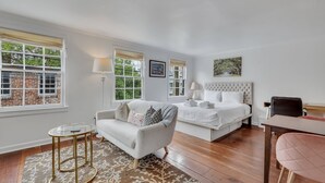A bedroom with a bed, a sofa, a small table, and a chair. There are windows with curtains, a lamp, and a picture on the wall. - Walk Everywhere From America's Most Beautiful Street by Lucky Savannah (Savannah)