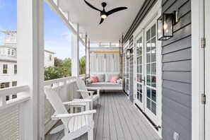 A covered porch with white railings, a ceiling fan, and a seating area with chairs and cushions.