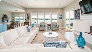 A spacious living room with a ceiling fan, a large TV, and a view of the outdoors.