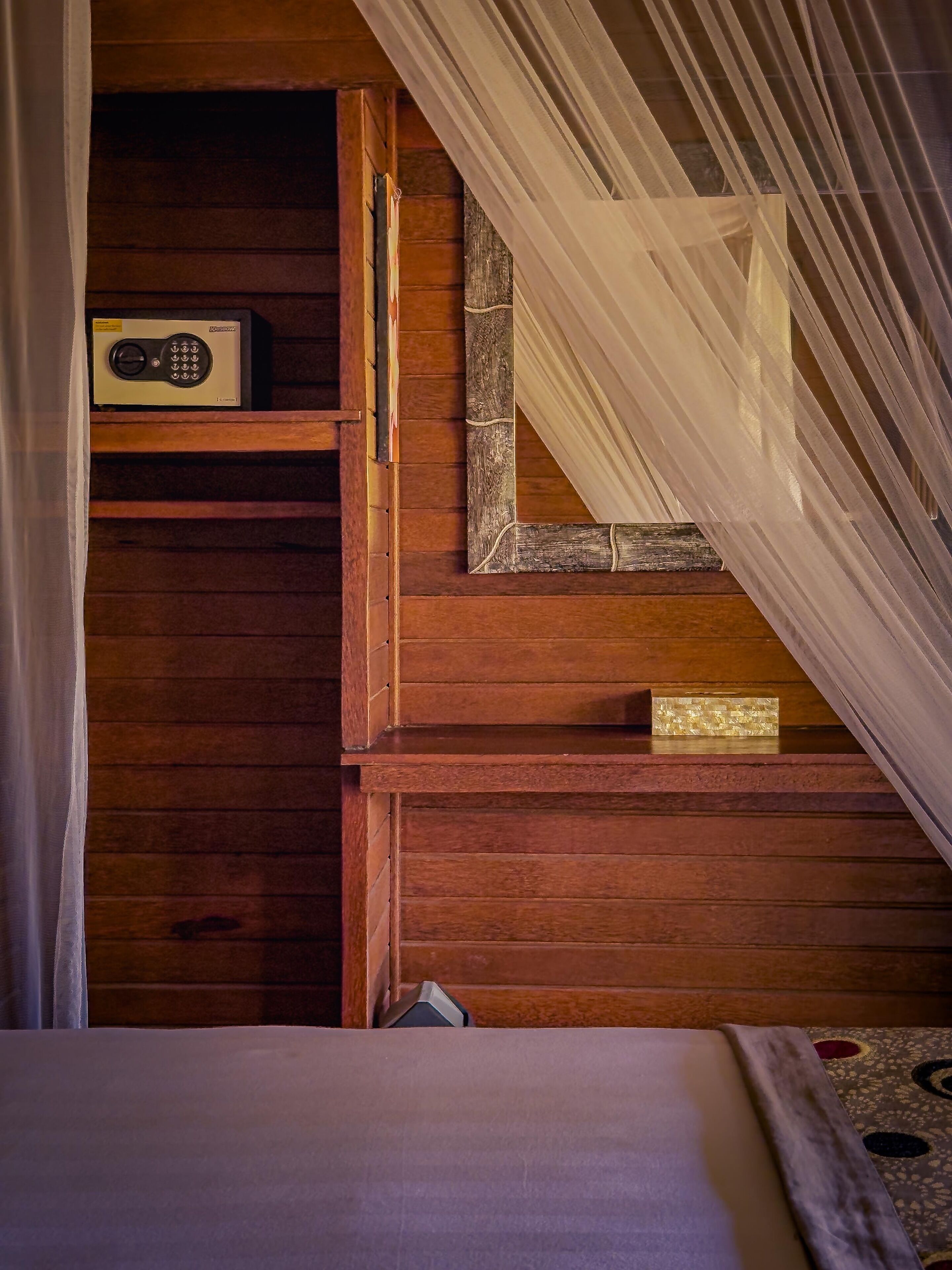 A wooden staircase with a small shelf holding a radio, a bed with a patterned bedspread, and sheer curtains.