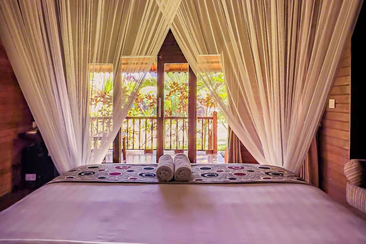 Una cama con dosel, un tapete estampado y vistas de vegetación al exterior.