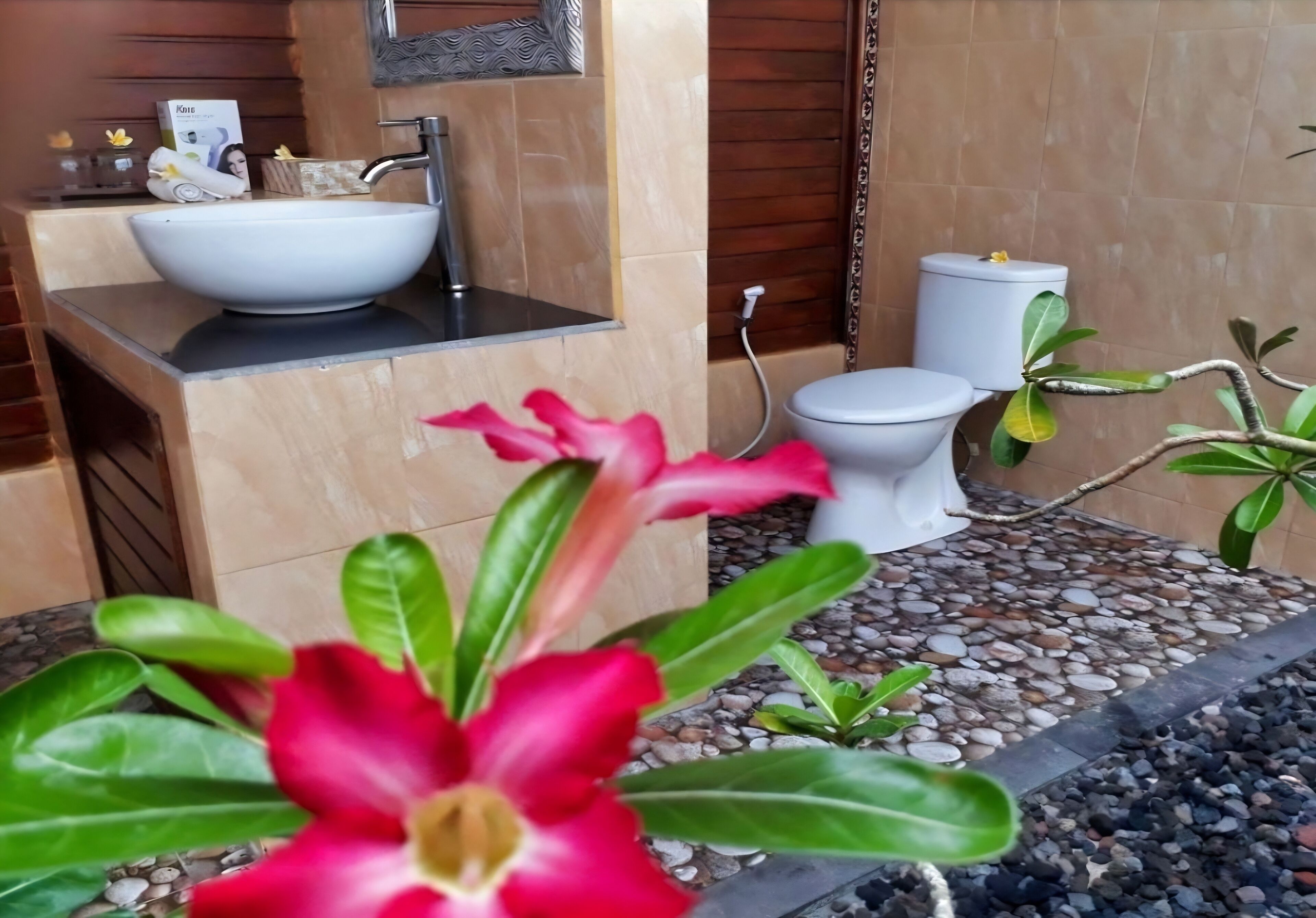 A bathroom with a white sink, toilet, and a shower area. There are plants and a decorative item on the counter.
