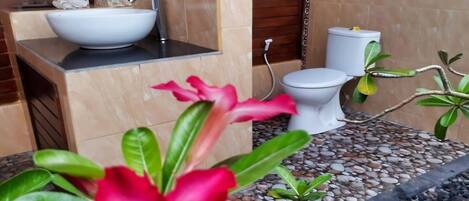 A bathroom with a white sink, toilet, and a shower area. There are plants and a decorative item on the counter.