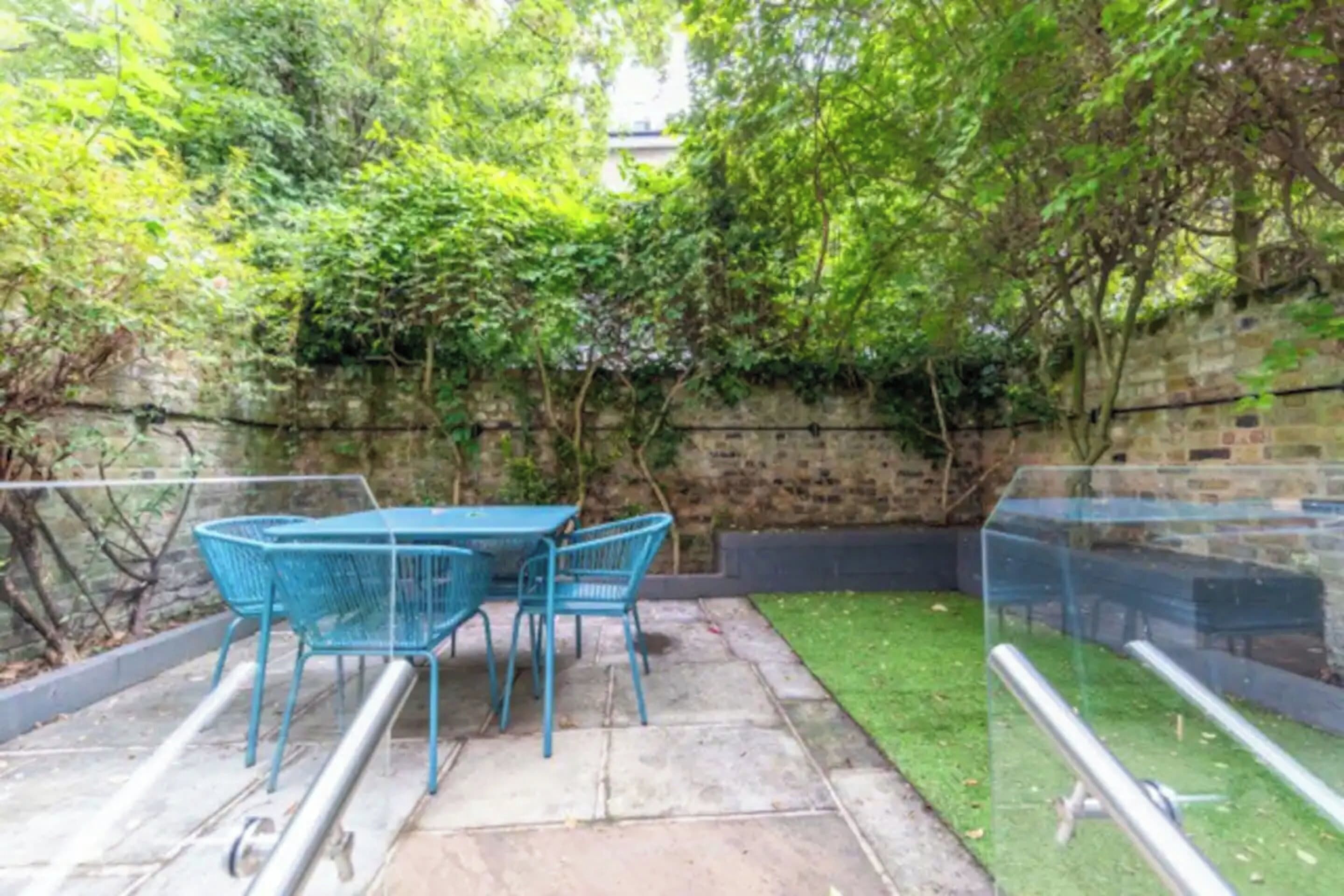 A patio with a table and chairs, surrounded by a brick wall and greenery.