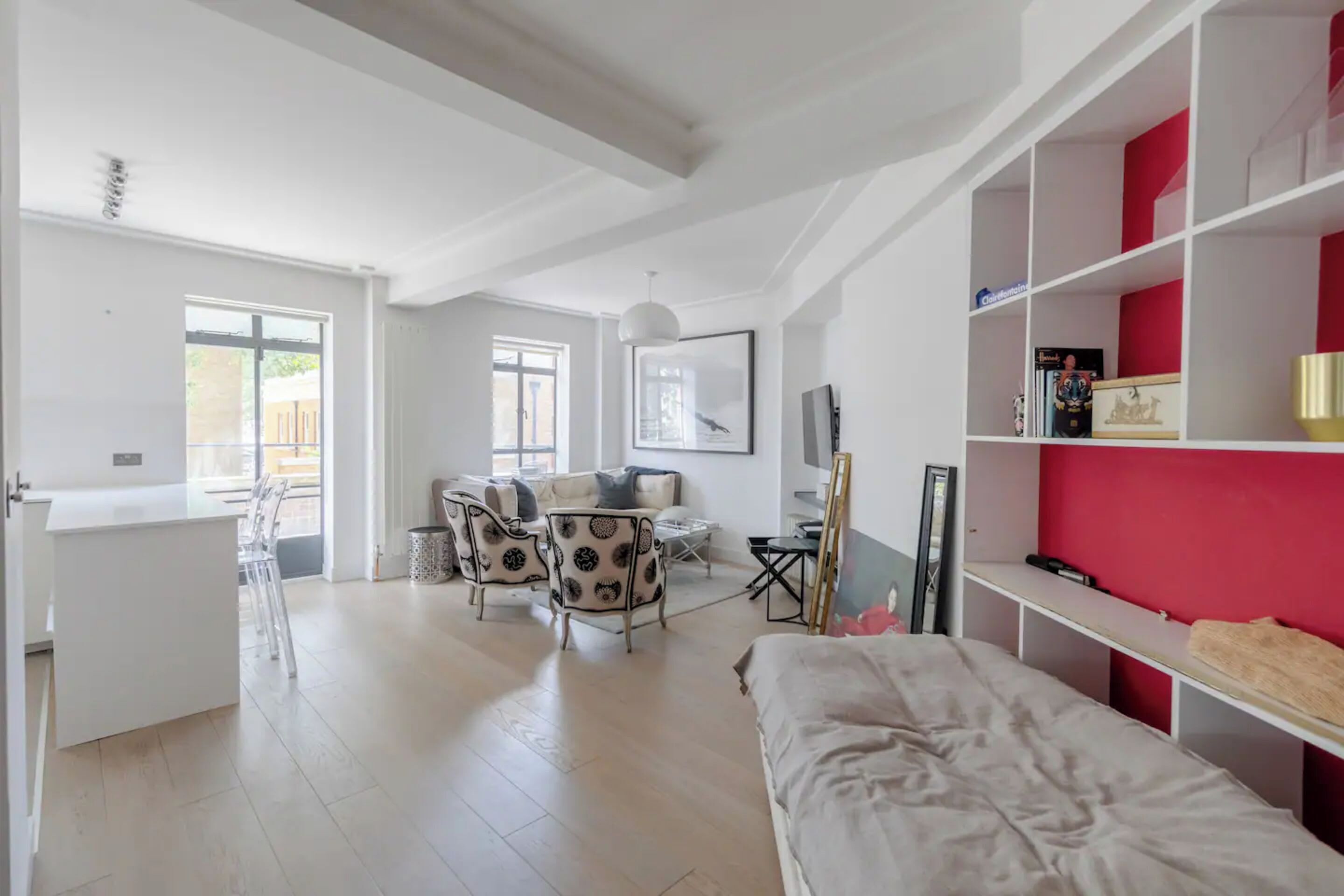 Una habitación moderna y luminosa con una cama, un comedor con sillas, un escritorio blanco y una pared de acento roja.