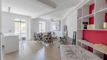 Una habitación moderna y luminosa con una cama, un comedor con sillas, un escritorio blanco y una pared de acento roja.