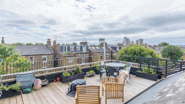 A rooftop terrace with a wooden deck, seating area, and potted plants. - Top Floor 1BD Flat With Balcony - Ladbroke Grove (London)
