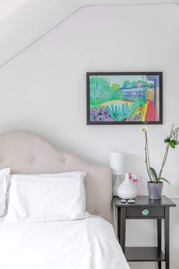 A bedroom with a bed, a nightstand, a lamp, and a framed painting of a garden scene. - Top Floor 1BD Flat With Balcony - Ladbroke Grove (London)