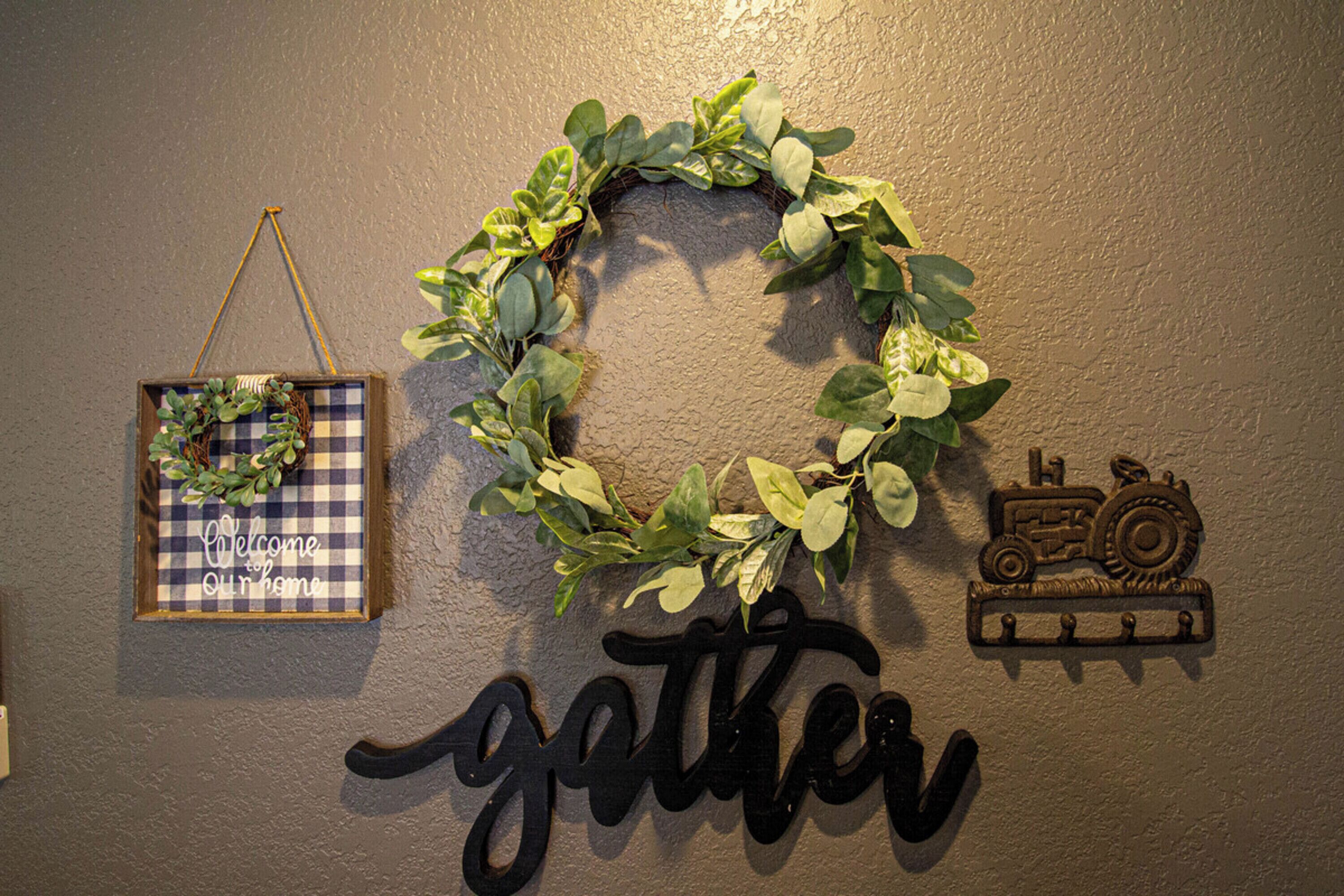 A wall with a wreath, a welcome sign, and a 'gather' sign.
