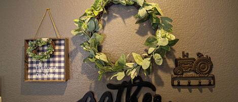 A wall with a wreath, a welcome sign, and a 'gather' sign.