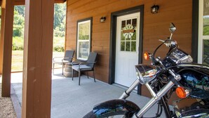 Een motorfiets staat geparkeerd voor een houten gebouw met een veranda, een deur met een 'Welcome'-bord en twee stoelen op de veranda.