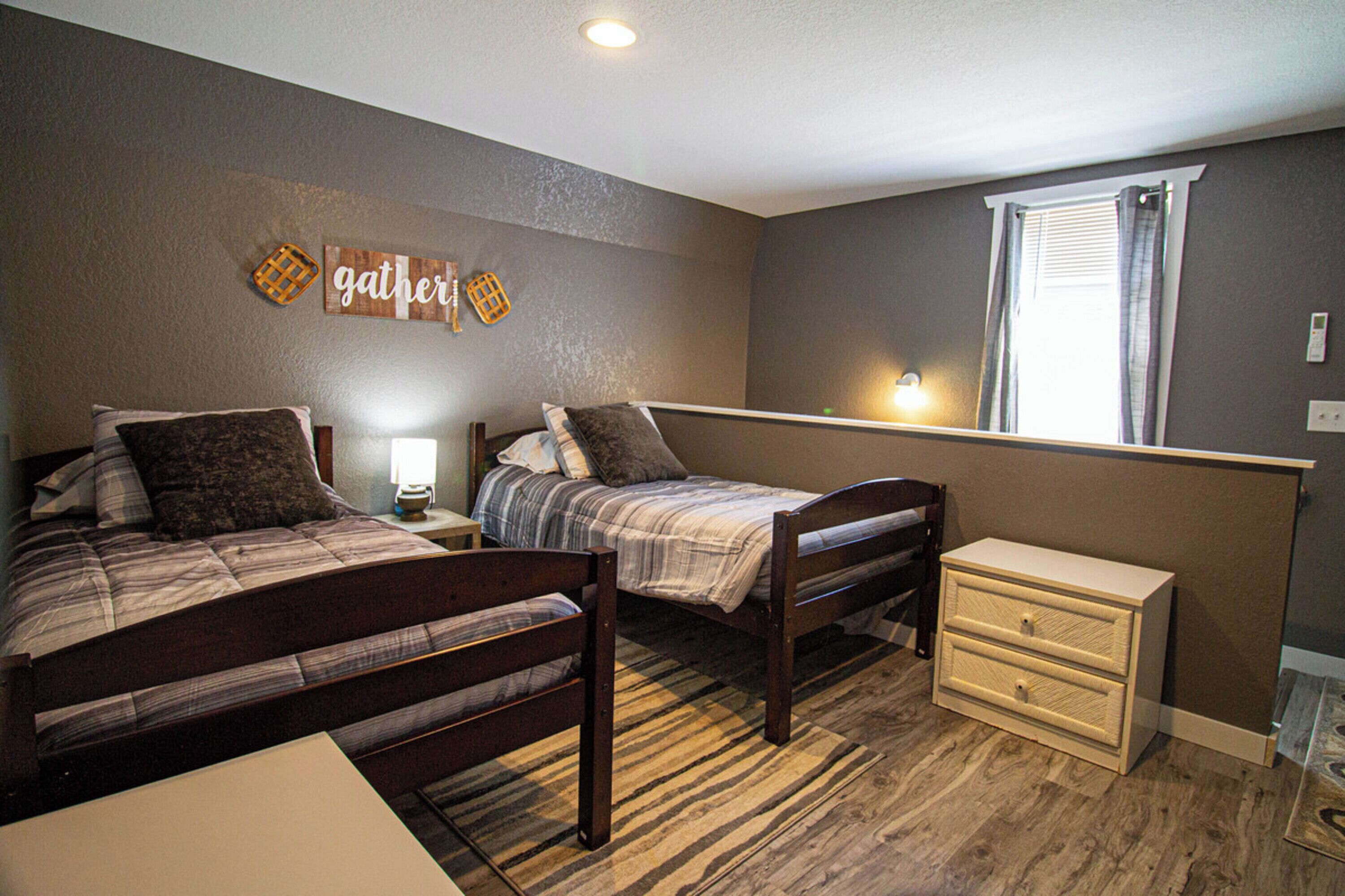 A bedroom with two beds, a nightstand, a dresser, and a window with blinds.