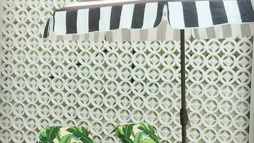 A white lattice wall, a striped umbrella, and two green lounge chairs with a potted plant.
