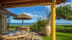 An outdoor dining area with wicker furniture, a thatched umbrella, and a view of the ocean. - Penthouse "Jewel" - Exquisite Pool View 2 bedroom - AC (Kapaa)