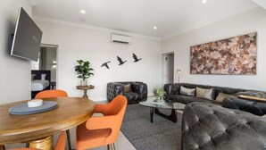 A modern living room with a sofa, a coffee table, and a dining area with chairs. - Sanlor Suite 2 | Luxury, Comfort & Style (Orange)