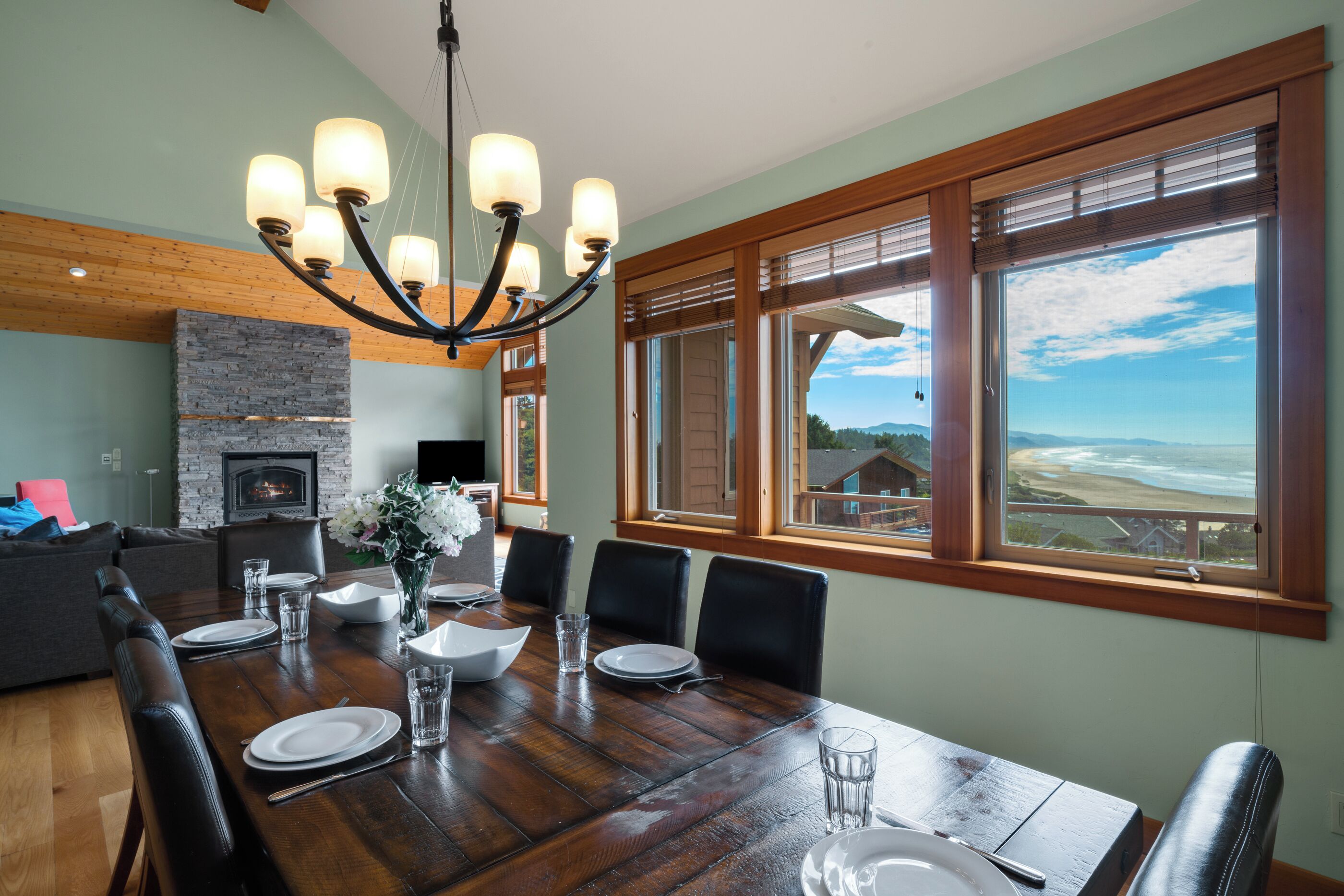 A dining area with a wooden table set for six, a fireplace, and a view of the beach.