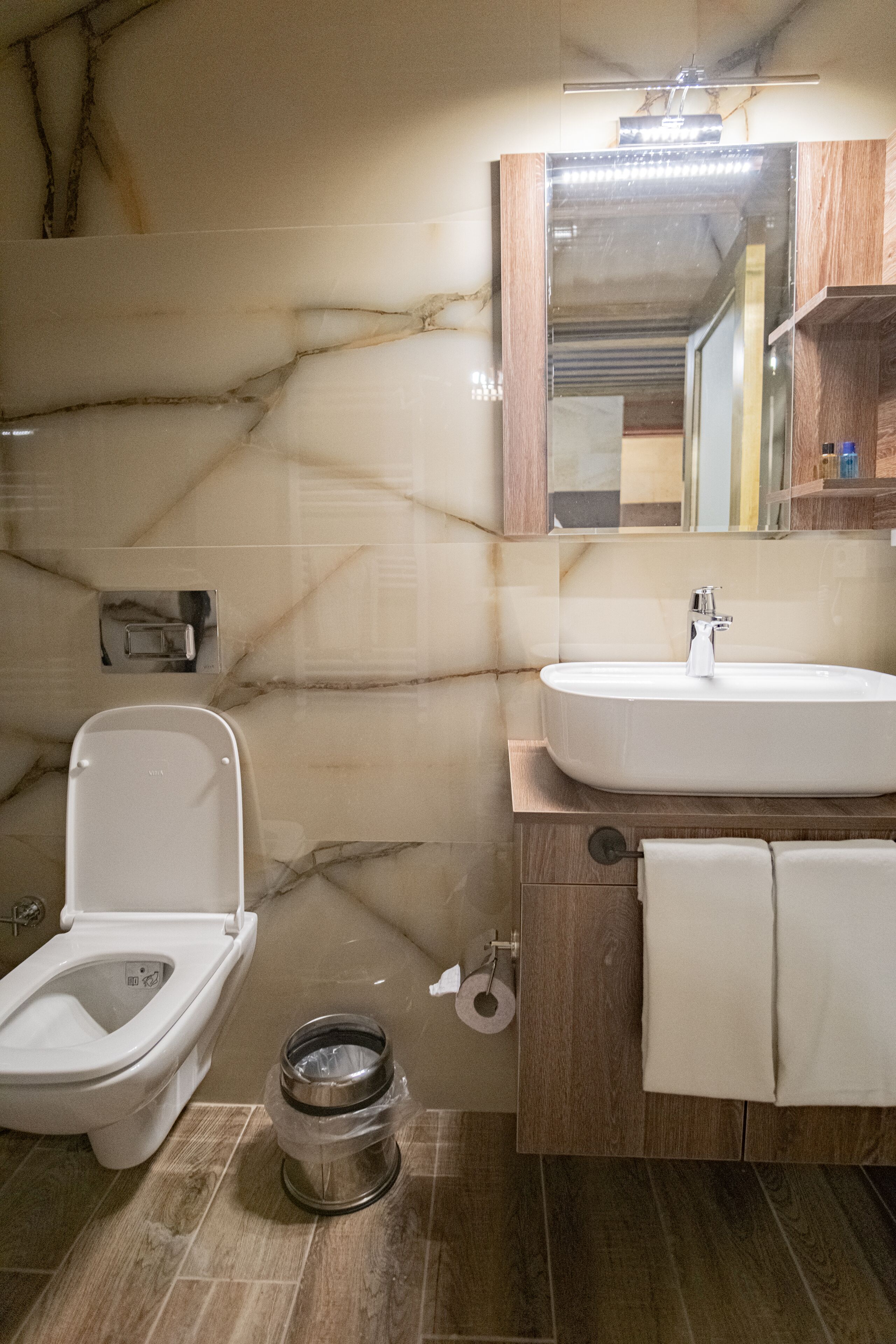 A bathroom with a marble wall, a toilet, a sink, and a mirror.