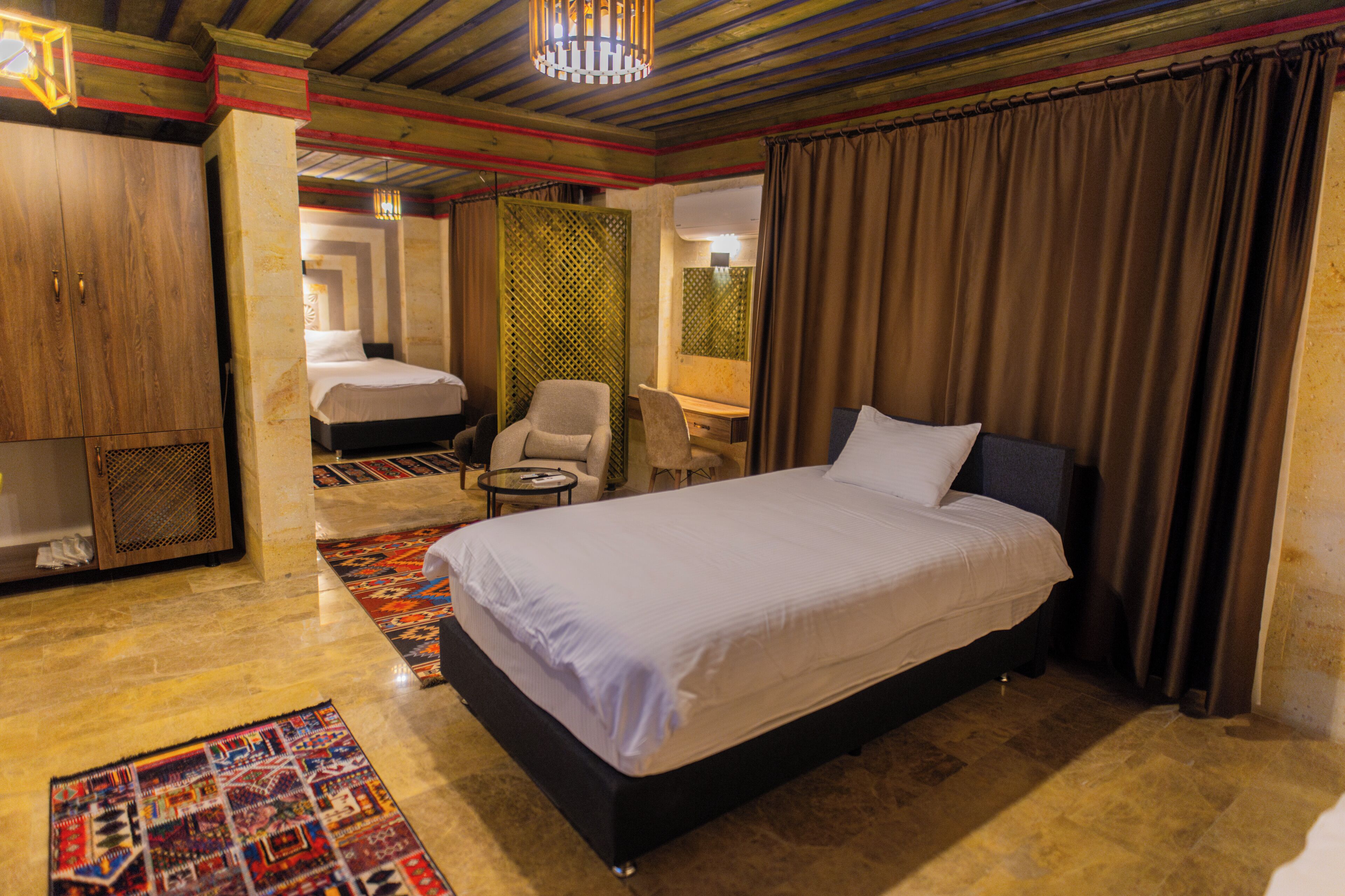 A hotel room with a large bed, a desk, a chair, a wardrobe, and a patterned rug.