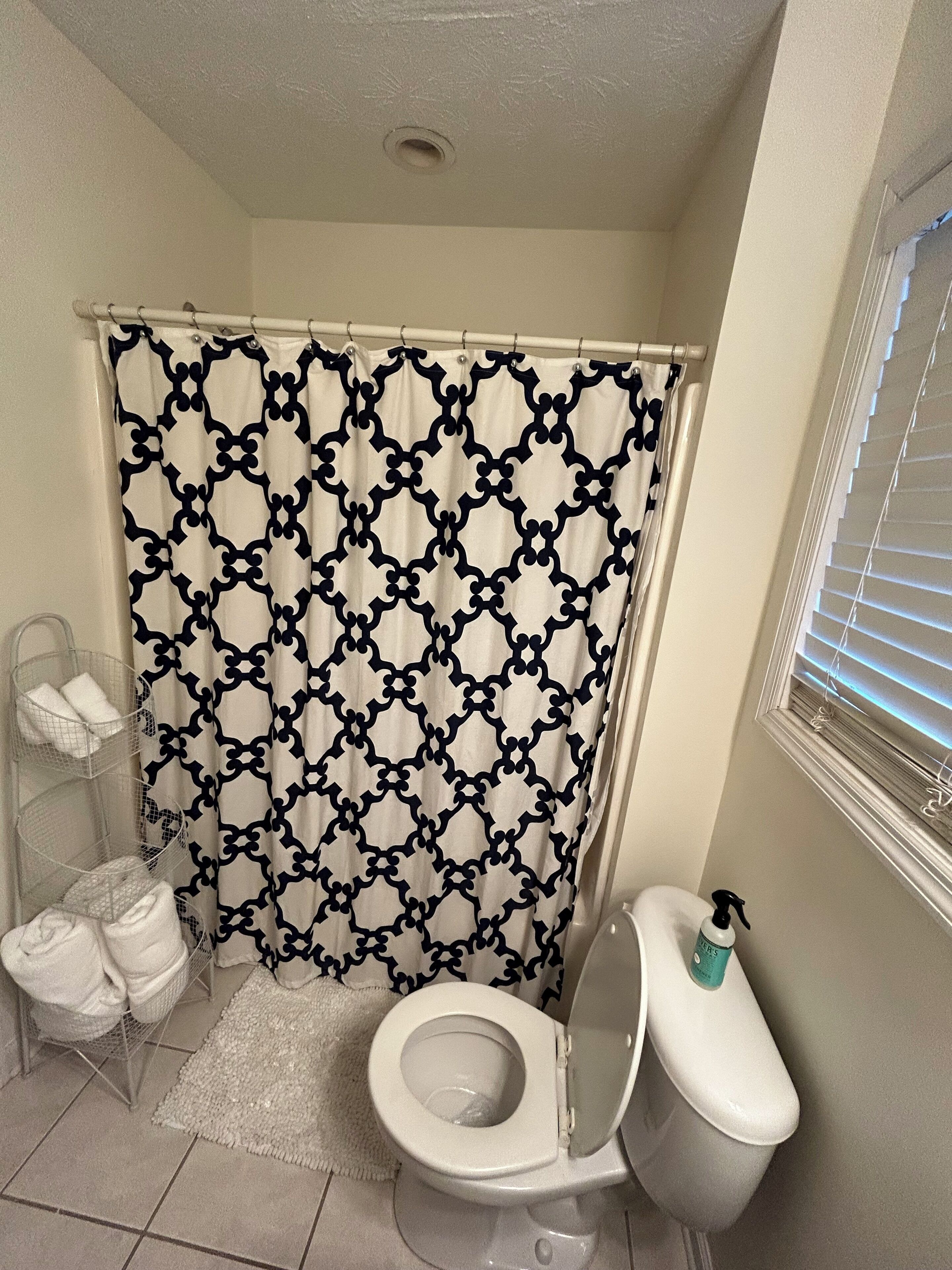 A bathroom with a patterned shower curtain, a toilet, a hand dryer, and a towel rack with towels.