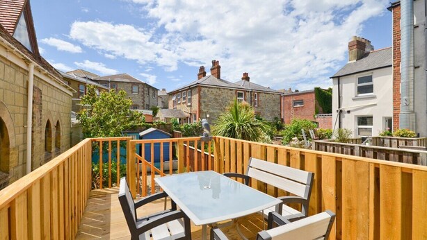A wooden deck with a glass table and chairs, surrounded by a wooden fence, overlooking a residential area with stone and brick houses. - Real hidden gem - Free all Island parking permit (Ventnor)