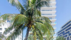 A modern building with multiple floors, surrounded by palm trees and a parking area with cars. - GA Ocean Villa  (Miami Beach)