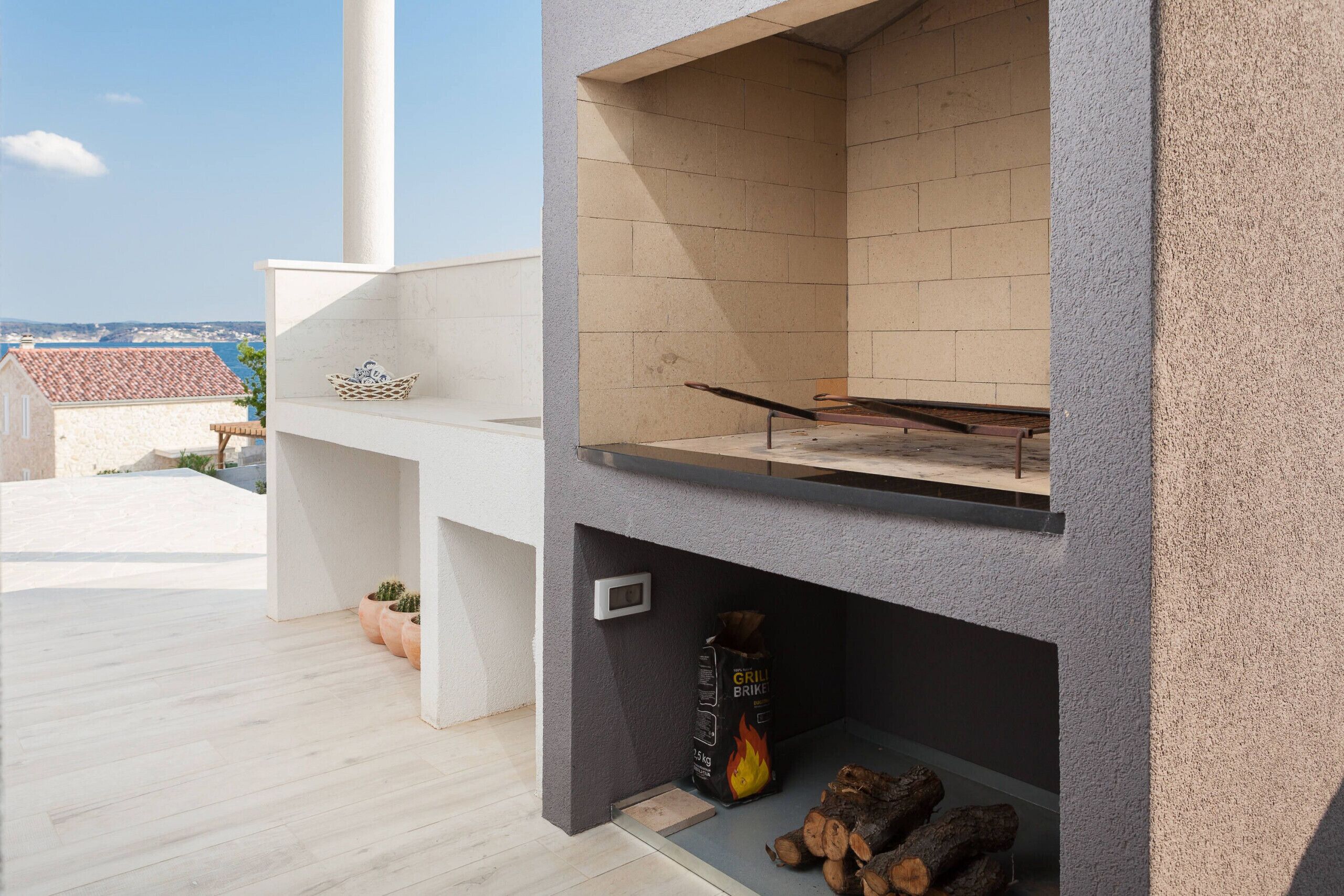 Un patio moderno al aire libre con zona de barbacoa integrada, un rincón de estar pequeño y vistas al mar.