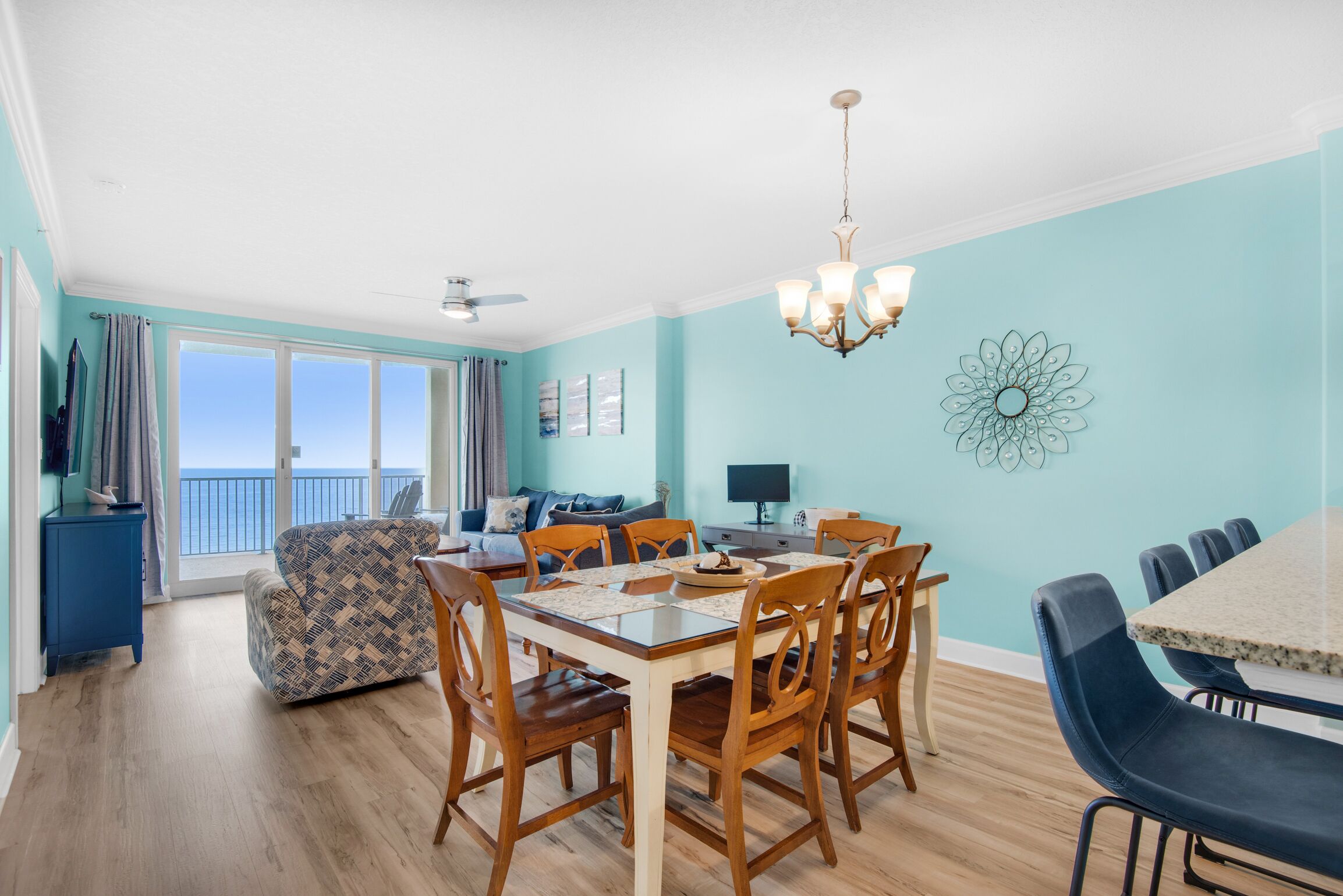 A dining area with a table and chairs, a chandelier, and a view of the ocean through large windows.