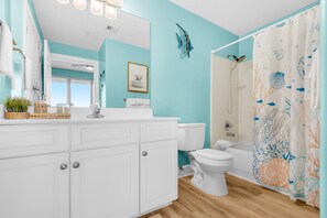 A bathroom with a white vanity, a toilet, and a shower with a decorative curtain.