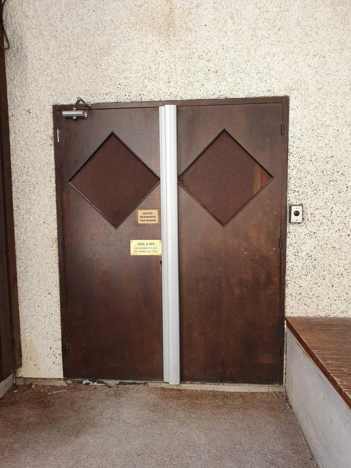 A double door with a metal handle and two diamond-shaped vents, a sign indicating access by badge, and a small plaque with text.
