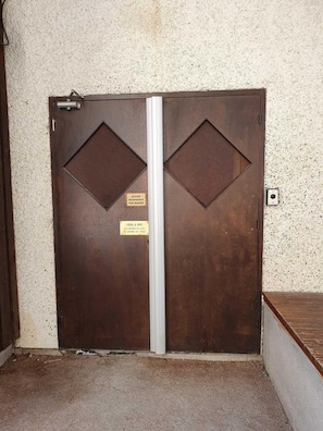 A double door with a metal handle and two diamond-shaped vents, a sign indicating access by badge, and a small plaque with text. - 100m from ski slopes, 7th floor, view open, balcony, fireplace or stove, ski locker, 32m², Les Orres (Les Orres)