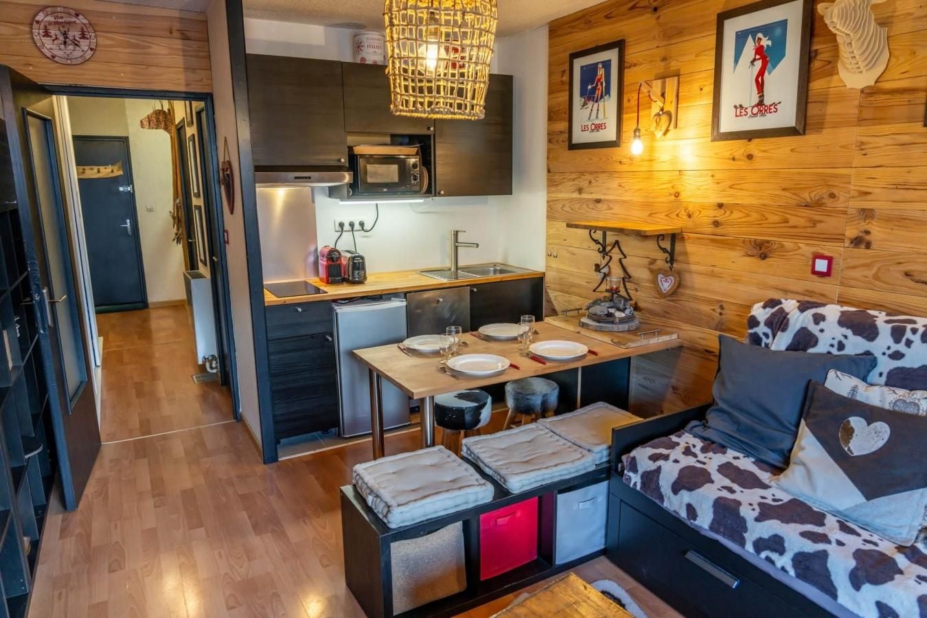 Un espacio habitable compacto con kitchenette, zona de comedor y sofá estampado con diseño de vaca.