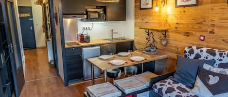 Un espacio habitable compacto con kitchenette, zona de comedor y sofá estampado con diseño de vaca.