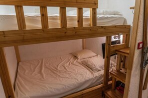 Una cama litera con una cama inferior y una cama individual. Hay un estante con una caja roja y un objeto negro encima.