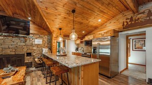 A kitchen with a stone fireplace, wooden ceiling, and stainless steel appliances. - Lakefront Oasis w/ Hot Tub, Pool, Courts & 2 Homes (Oakland)