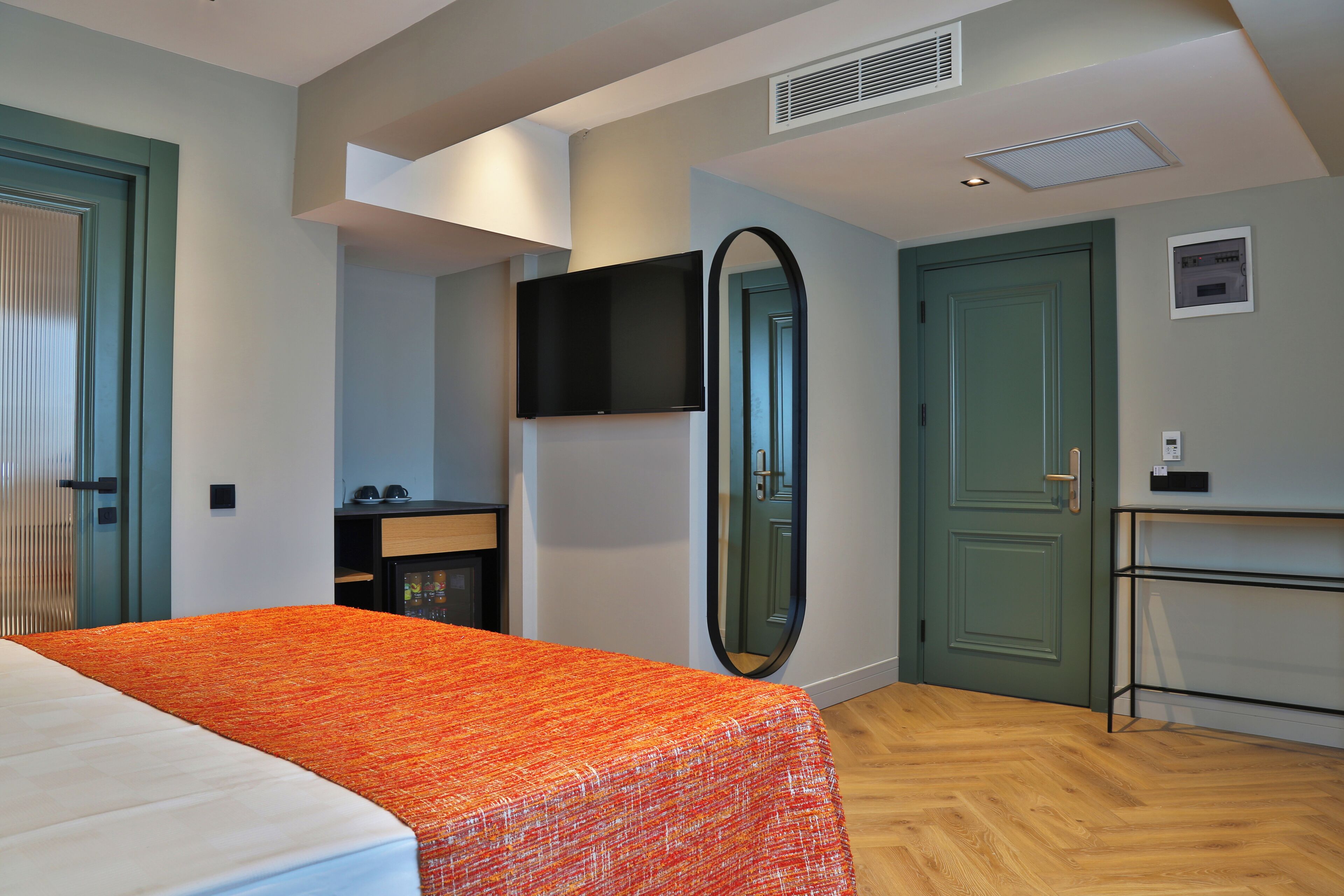A bedroom with a bed, a desk, a mirror, and a wardrobe.