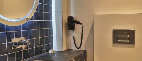 A modern bathroom with a marble sink, a large mirror, a towel rack, a toilet, and a hand dryer.