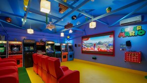 A colorful arcade room with multiple gaming machines, red seating, and a large screen displaying a Mario game. - 🕹️🎬🏎️👾Gamers Getaway: Arcade ,Theater, Racing, And More! (Fullerton)