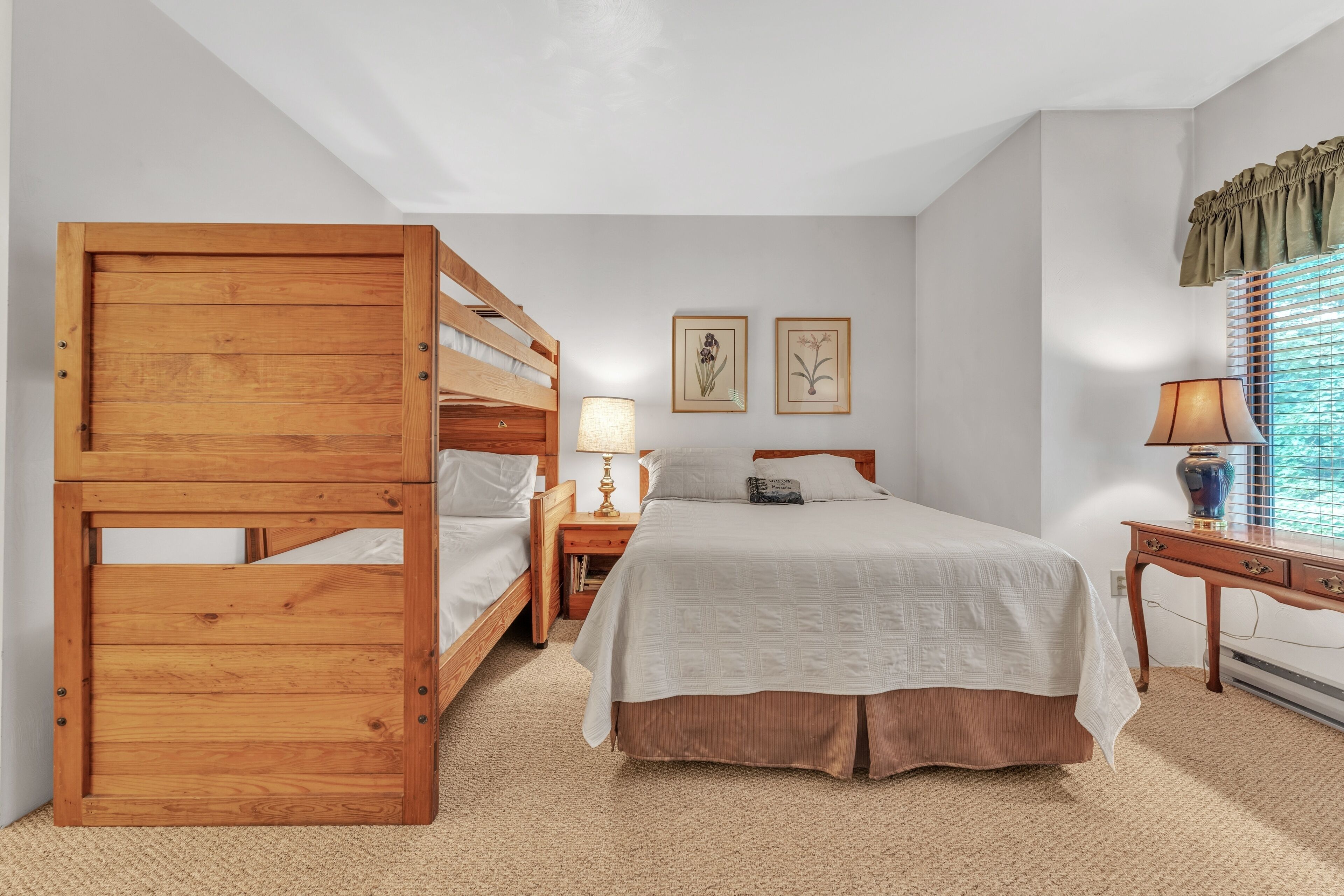Quarto com uma cama de solteiro, uma cama individual, uma mesinha de cabeceira com abajur, e duas gravuras botânicas emolduradas na parede.