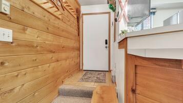 A wooden interior hallway with a white door, a small rug, and a bench.