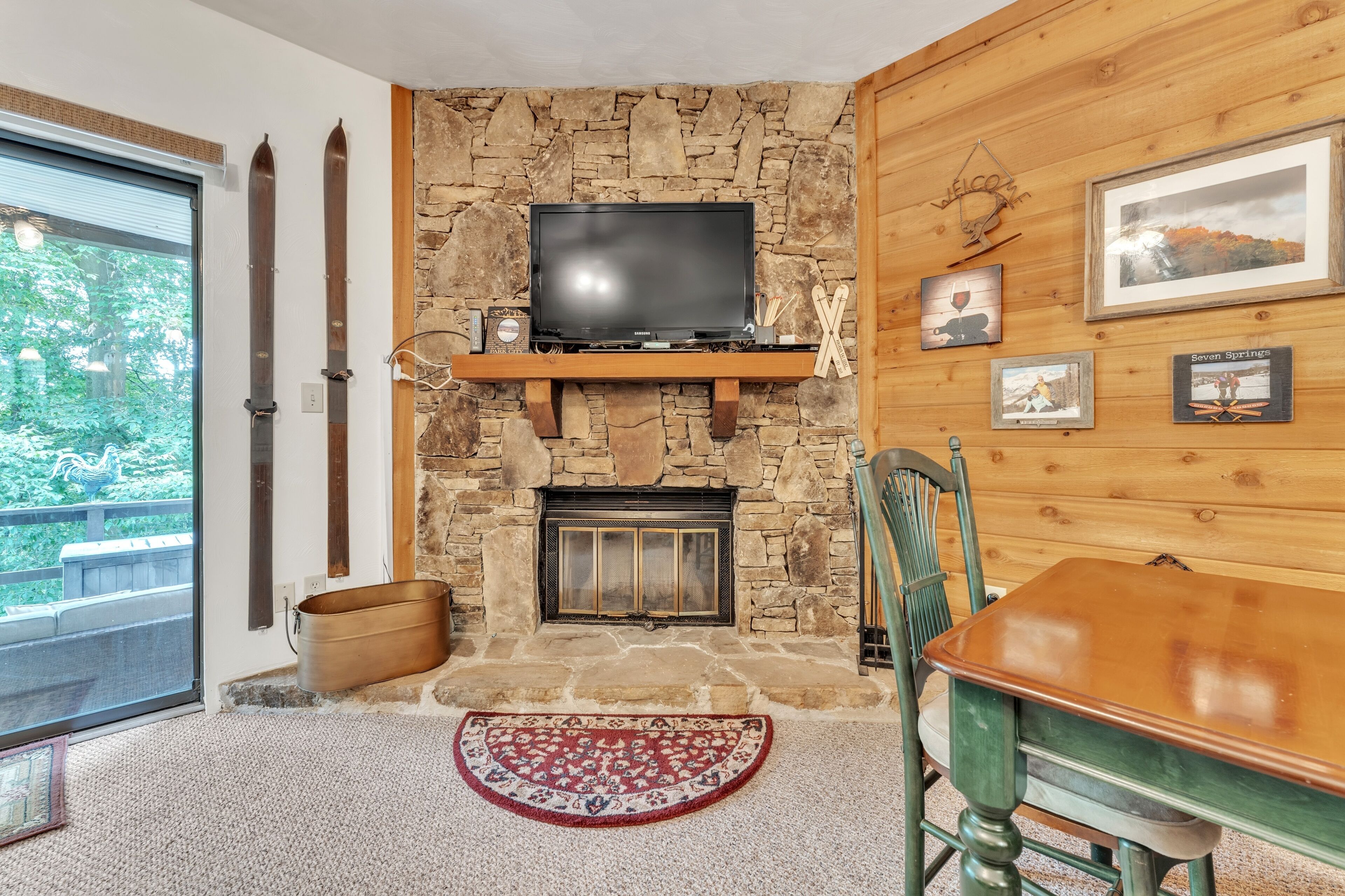 A cozy room with a stone fireplace, a mounted TV, and wooden walls.