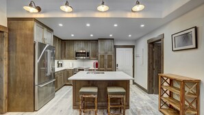A modern kitchen with wooden cabinets, stainless steel appliances, and a central island with stools. - Fully Renovated 2 Bedroom in Arrowhead Village! 2 Condo by RedAwning (Edwards)