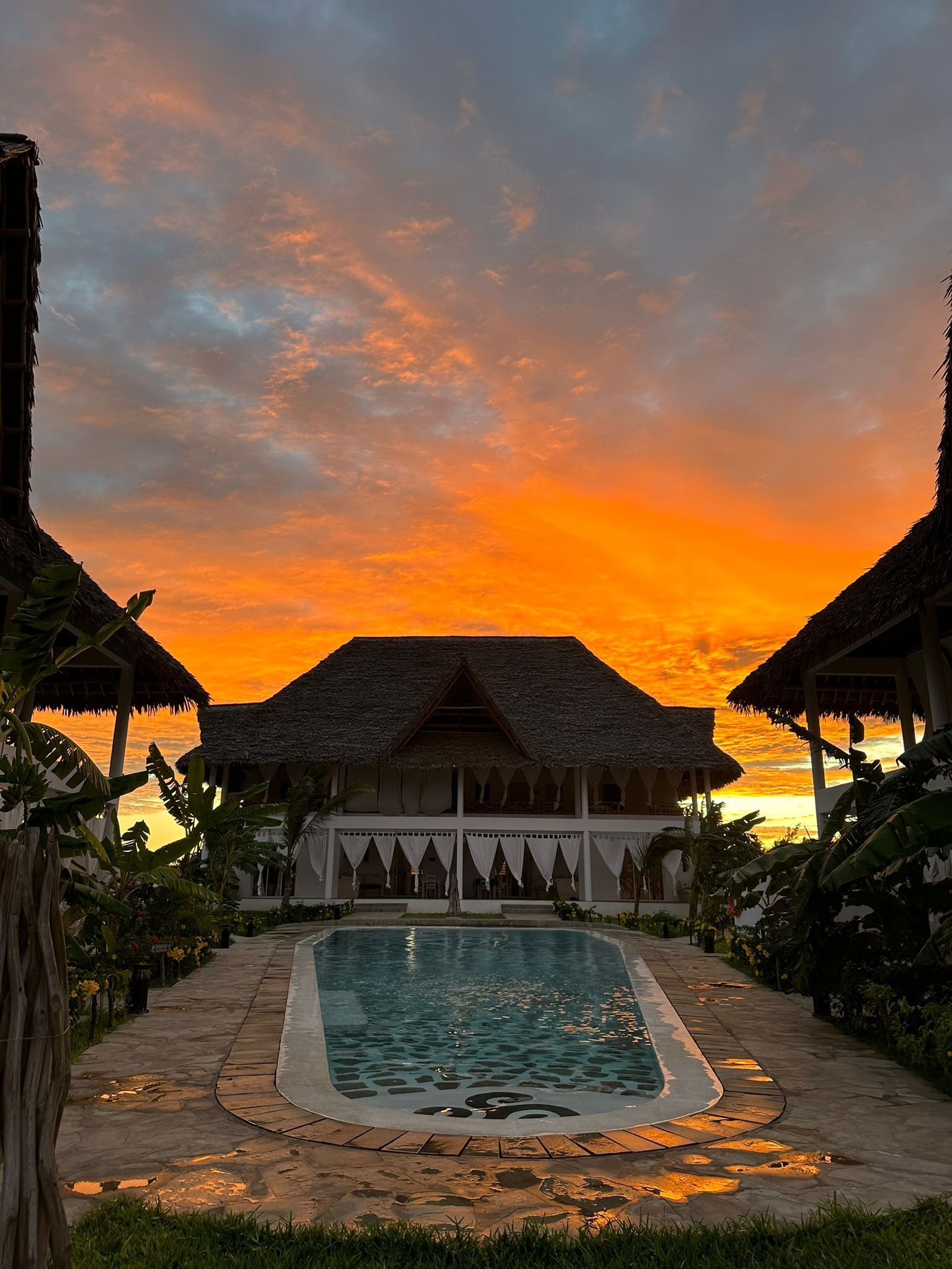 A resort with a pool, thatched-roof buildings, and tropical vegetation.