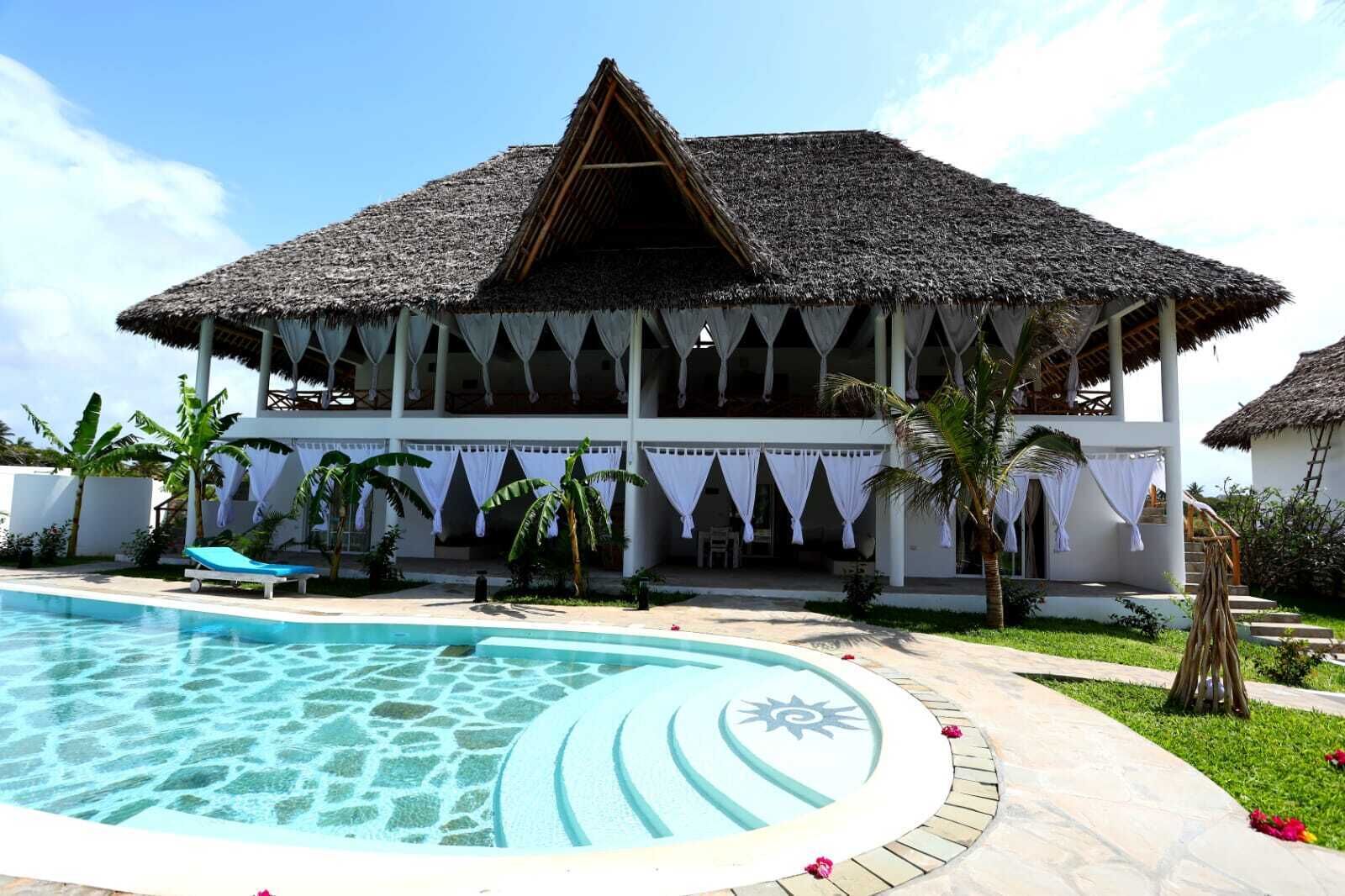 A resort with a pool, a thatched-roof building, and palm trees.