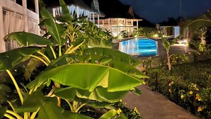 A pool area with a thatched-roof building, lush greenery, and a mountain backdrop. - Rafiki Tamu Residential Resort (Watamu)