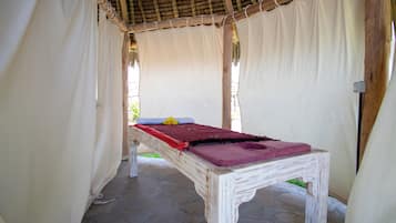 A single bed with a wooden frame and a red blanket, set in a room with white curtains and a thatched roof.