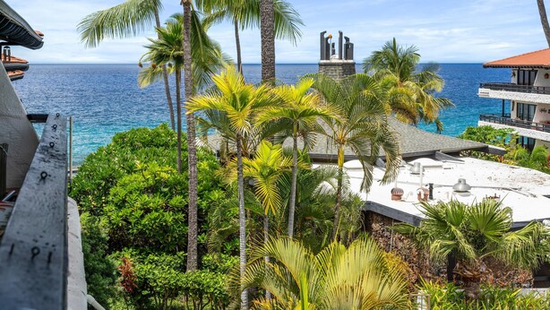 A view of a hotel with a pool, palm trees, and a clear blue sky. - Big Island Casa De Emdeko A308 1 Bedroom Condo (Kailua-Kona)